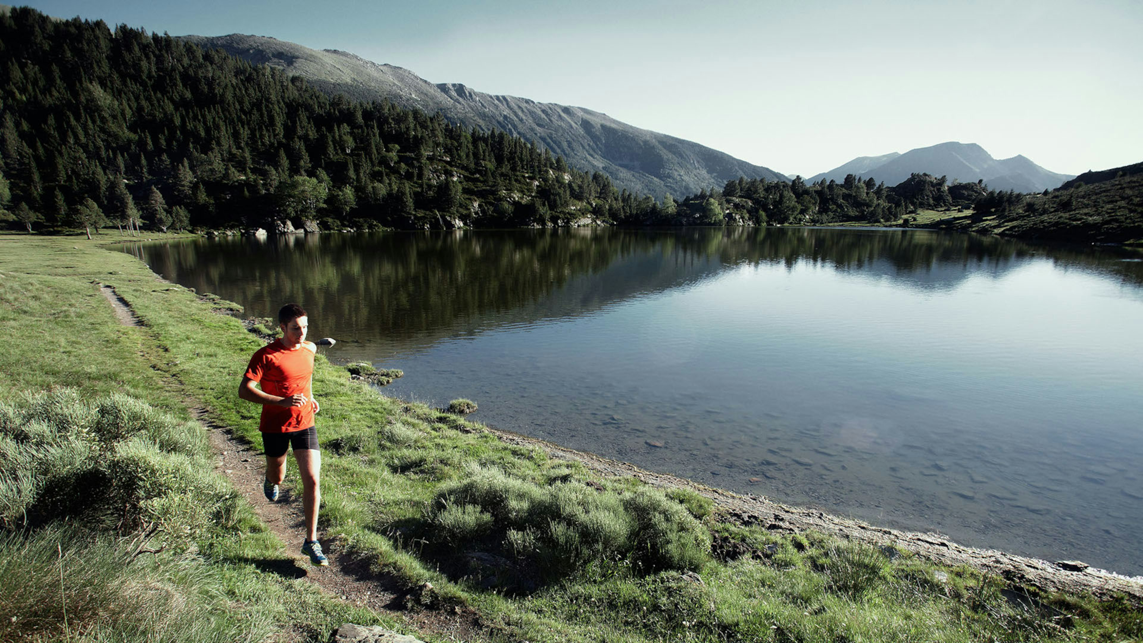 Ein Trailrunner läuft vor bergiger Kulisse am See entlang