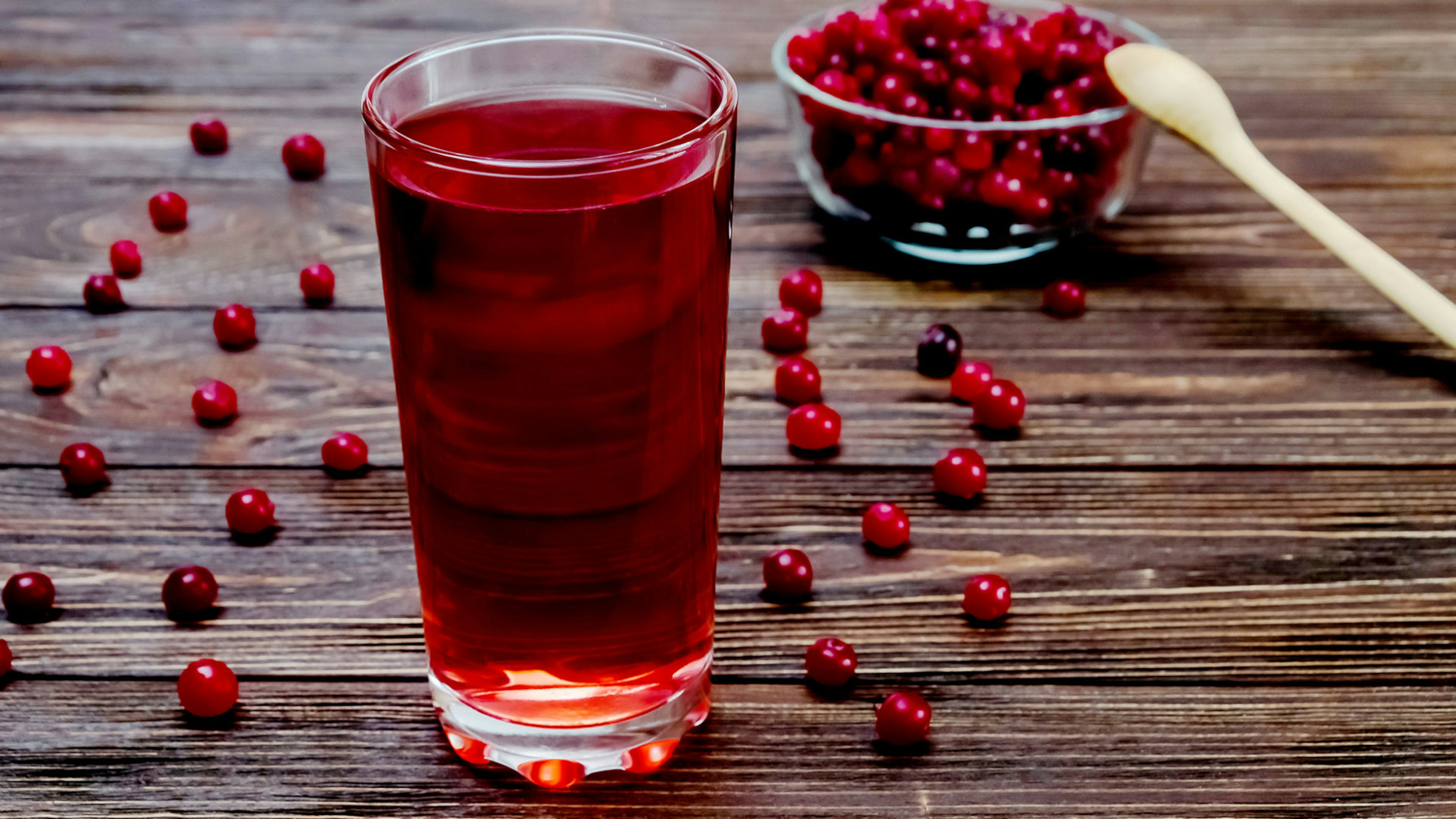 Ein volles Glas Cranberrysaft steht auf dem Tisch vor herumliegenden Beeren und einer Schüssel voll mit Cranberries