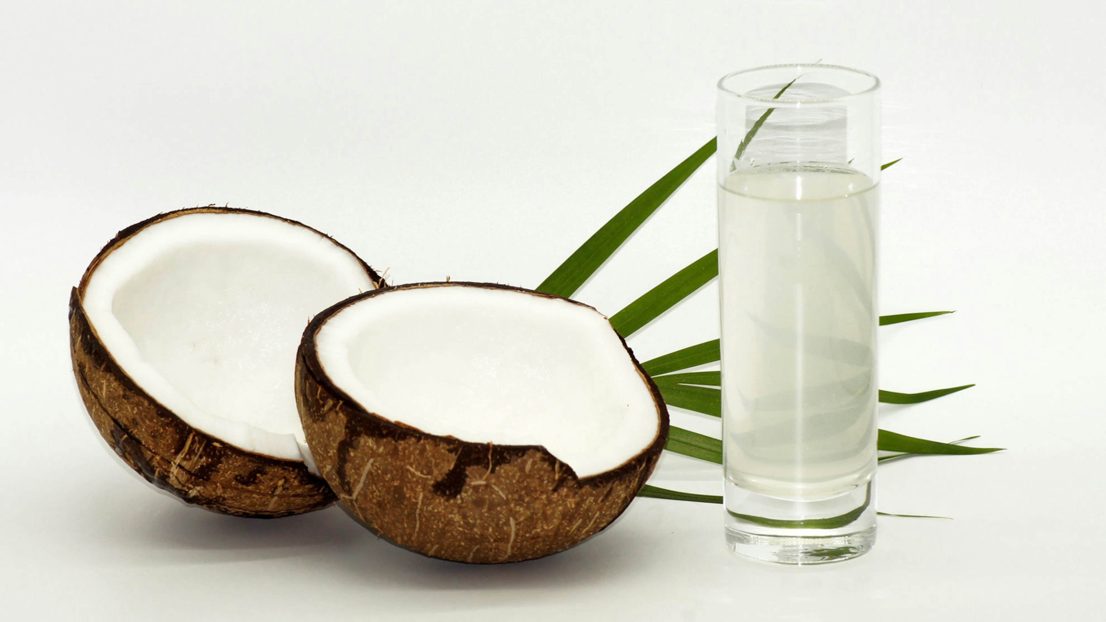 Eine geöffnete Kokosnuss liegt neben einem Glas voller Kokoswasser