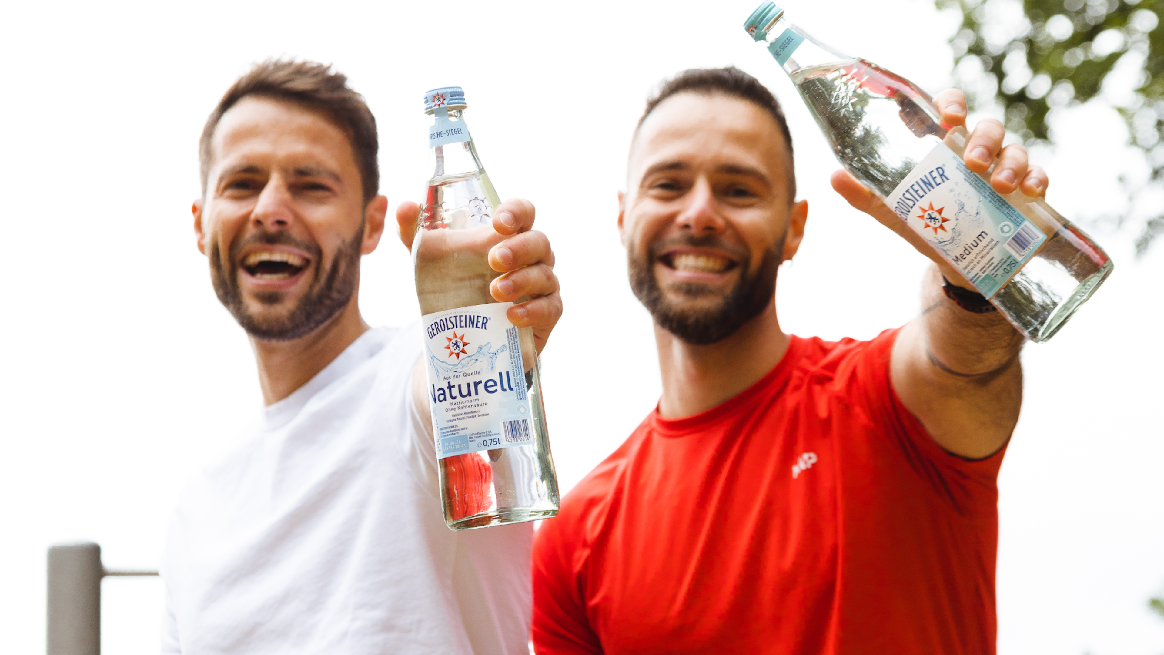 Zwei Männer in Sportkleidung halten zwei Flaschen Gerolsteiner Mineralwasser in die Kamera und lachen