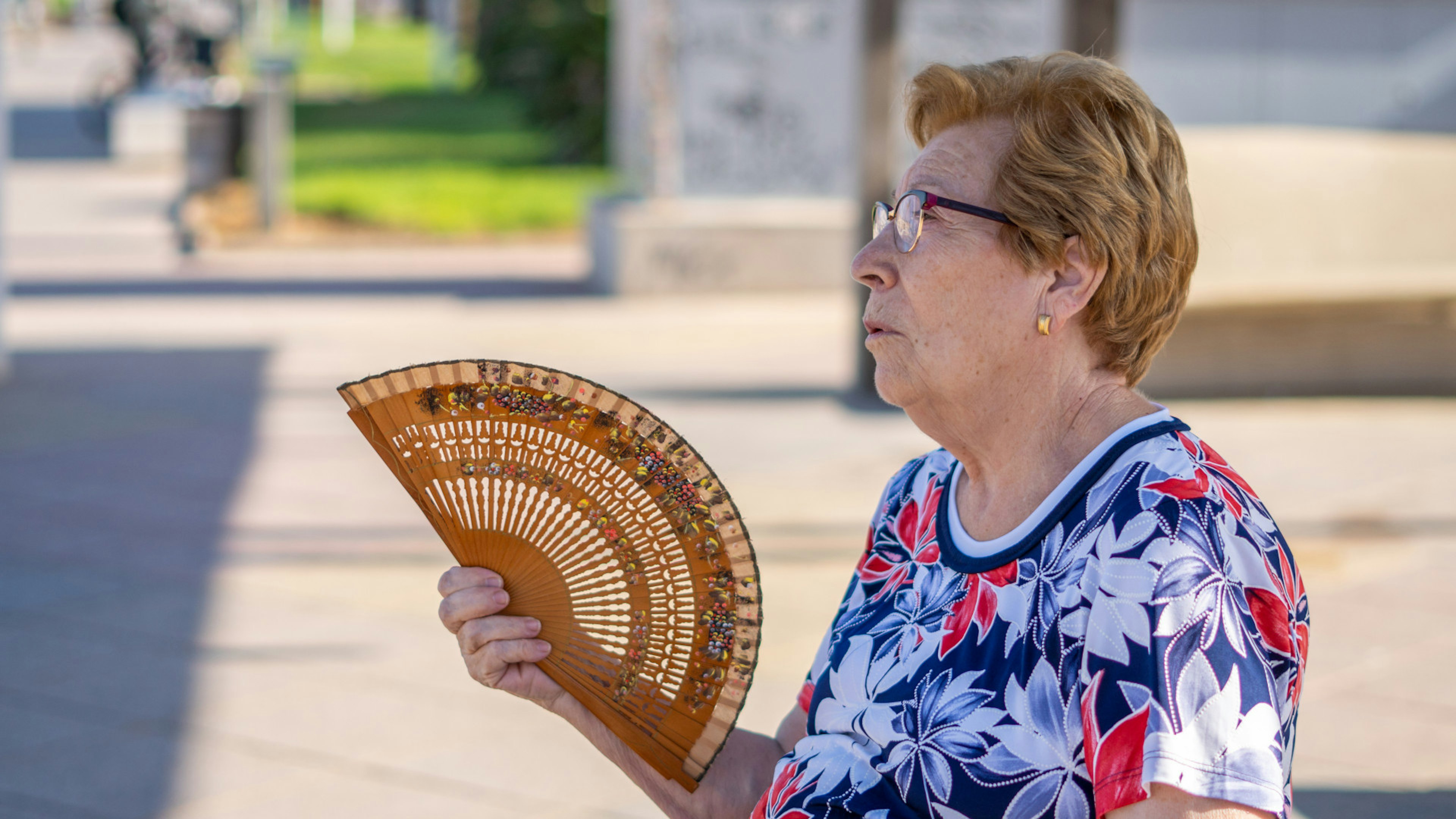 Eine ältere Frau in der Stadt, sie fächert sich mit einem Fächer Luft zu. Es ist heiß