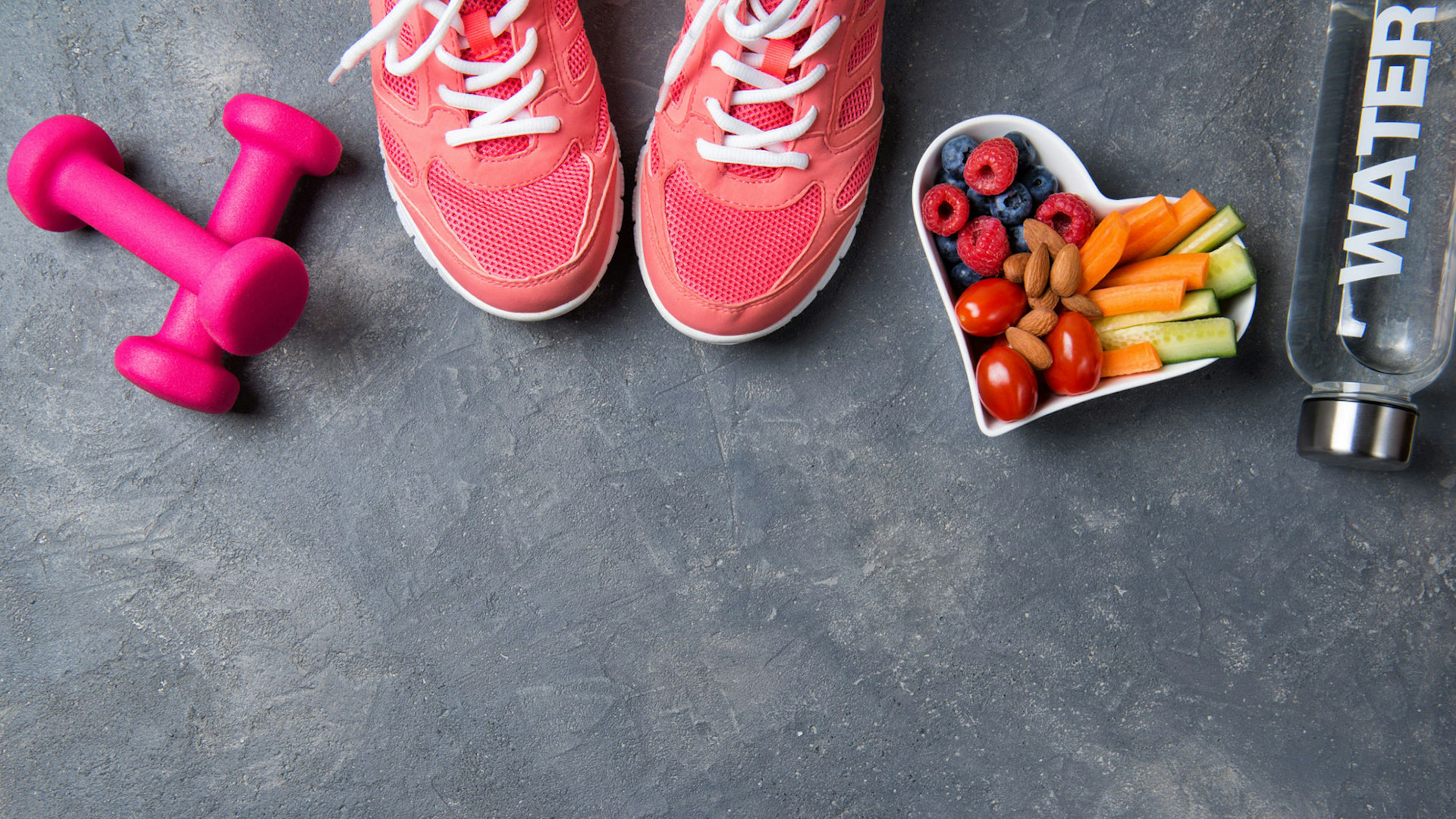 Pinke Sneakers und Hanteln, Wasserflasche und Schale mit Gemüse, Nüssen und Obst von oben fotografiert
