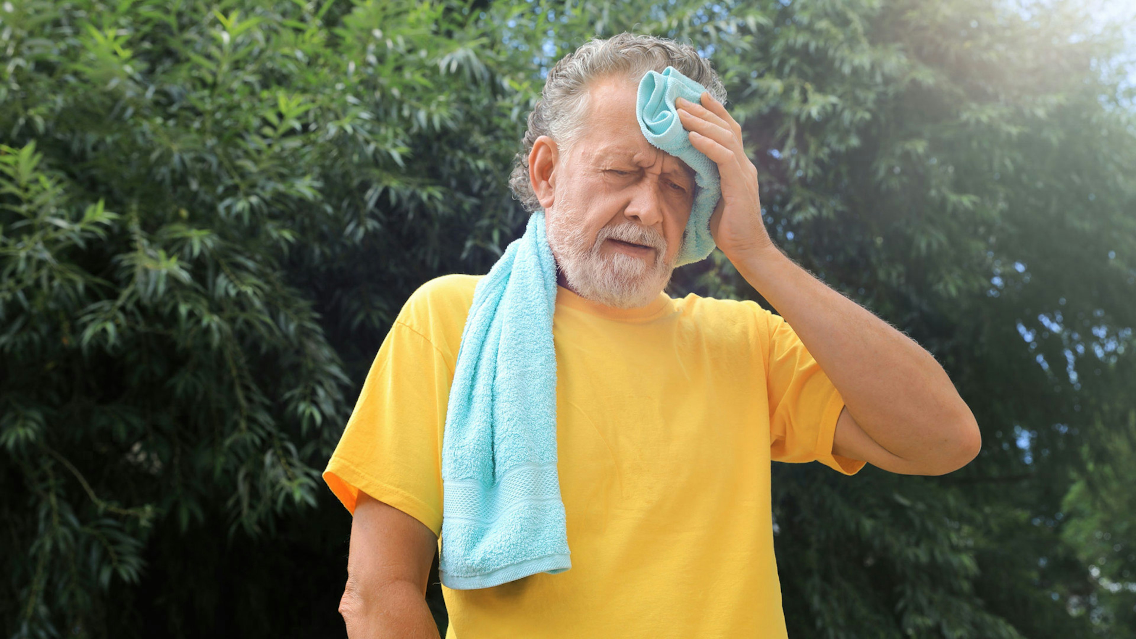 Ein älterer Mann im gelben T-Shirt wischt sich wegen Überhitzung den Schweiß von der Stirn